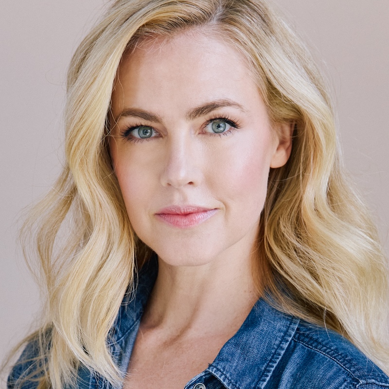 Headshot of Amanda Schull, a caucasian woman with blue eyes and blond hair. She wears a jean jacket and is in front of a beige background.