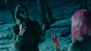 In a dark snowy landscape, two figures mirror each other with their hands raised. One has a short, bubblegum pink bob. The other looks otherworldly with a pale face, dark markings around their glowing eyes, and tattered clothing. Their hands glow dimly.