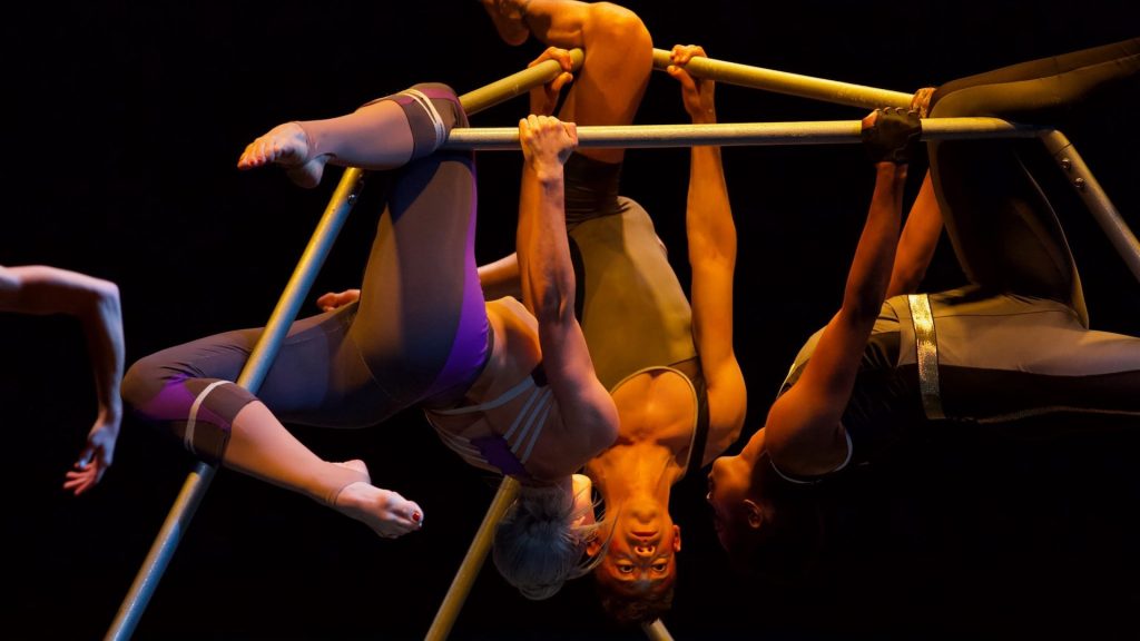 Dancers hang upside-down from a metal structure