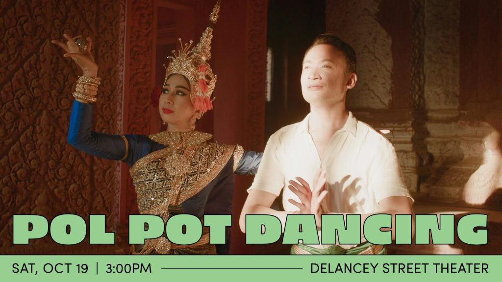 A Cambodian dancer poses with his palms pressed together in front of him, fingers splayed. He wears a white collared shirt and a bright light shines on his face. Behind him is another Cambodian dancer wearing an ornate costume, gold bangles, and an elaborate gold headdress. Her left arm is extended in front of her, forearm bent upwards at a 90 degree angle, with her splayed fingers holding a shiny ball.