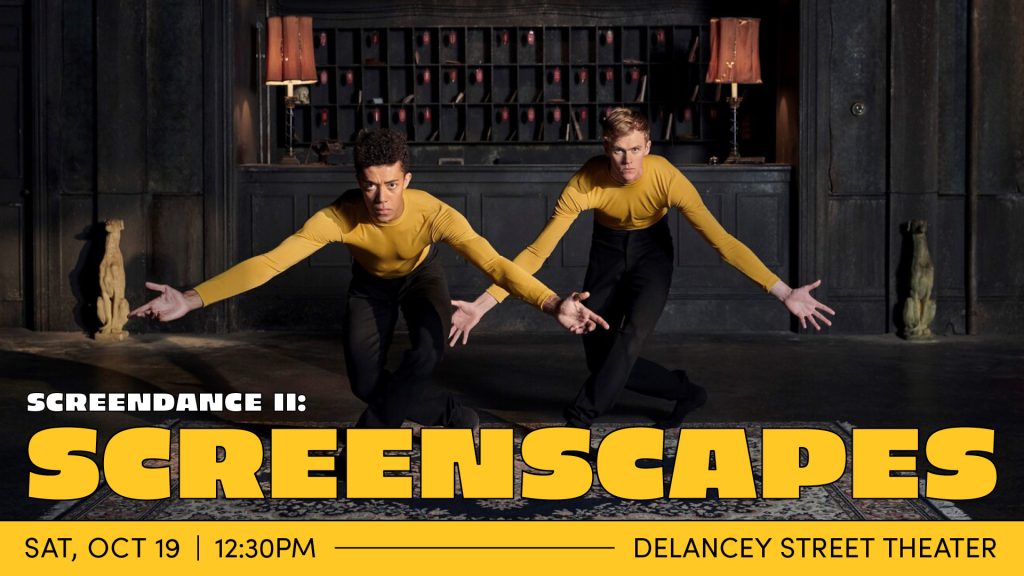 Two dancers in yellow long sleeved shirts and black pants are in a dark hotel lobby. Behind them is a worn black wall with cubbies, a clock, two mauve old fashioned table lights, and two small dog statues. The dancers are posed identically: bowed forward with their legs crossed and hands extended to their sides.