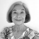 Headshot of Judy Flannery, a Eurasian woman with a gray bob. She is wearing a grey and white shirt.