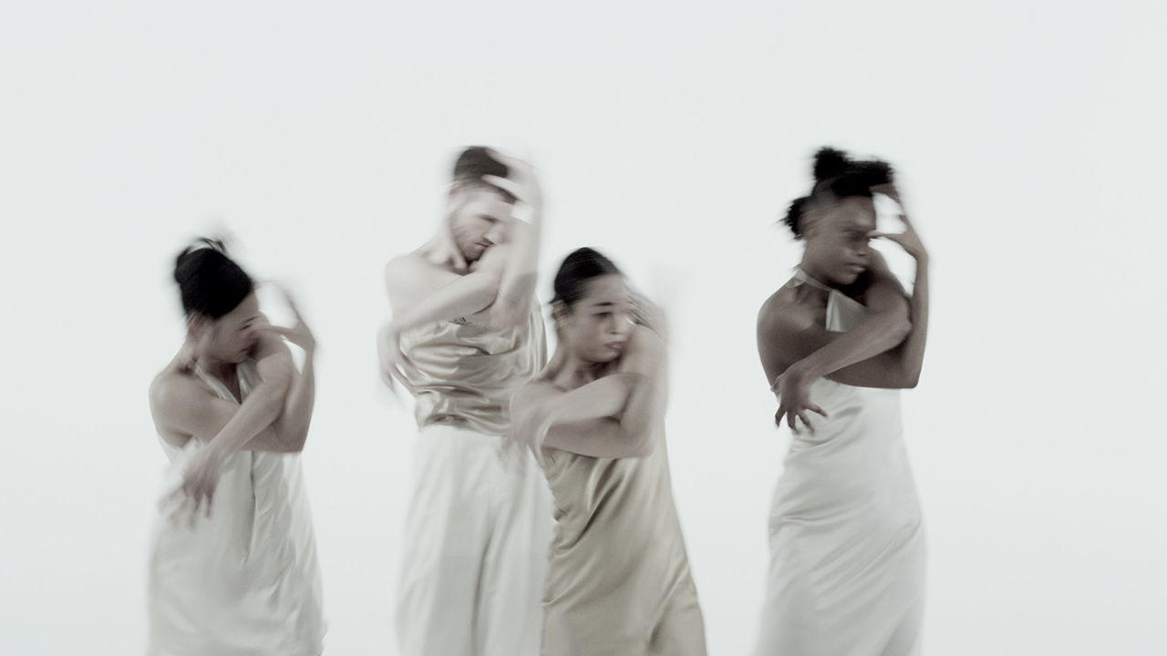 Four dancers in beige and white satin outfits stand in the same pose with their arms twisted around one another, one arm coming up towards their face and the other reaching down towards their waist. Their motion is heavily blurred. The background is flat and completely white. Four dancers in beige and white satin outfits stand in the same pose with their arms twisted around one another, one arm coming up towards their face and the other reaching down towards their waist. Their motion is heavily blurred. The background is flat and completely white.