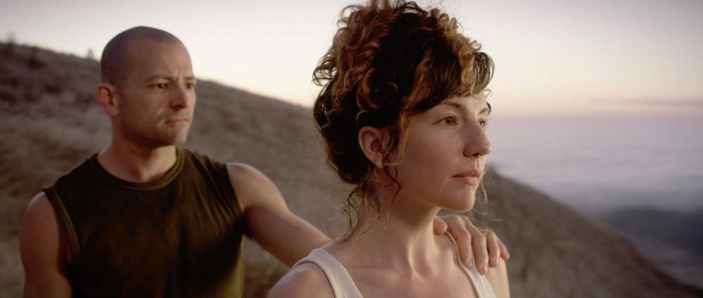 Film still from "The Space in Between" in which Private Freeman places a hand on the shoulder of Anna Greenberg who is turned away from them. They stand on a hillside.