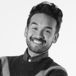 Chris is an Asian/Caucasian mixed male with short black hair, tan skin, and a black five o'clock shadow. He smiles in front of a white background and is wearing a dark dress shirt with a Chevron patterned knit sweater.